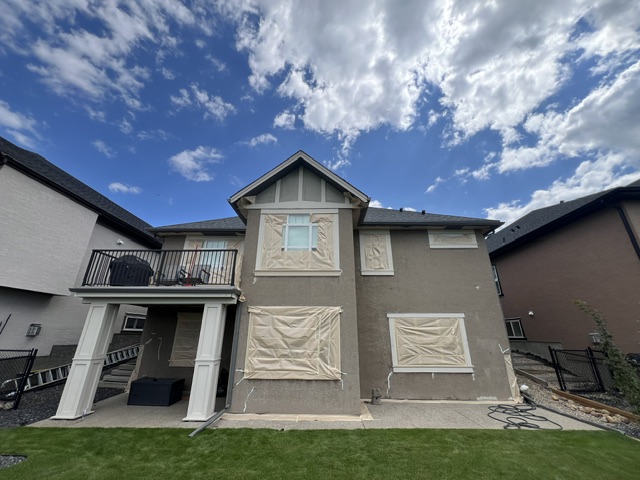 Brown stucco home with windows masked before painting